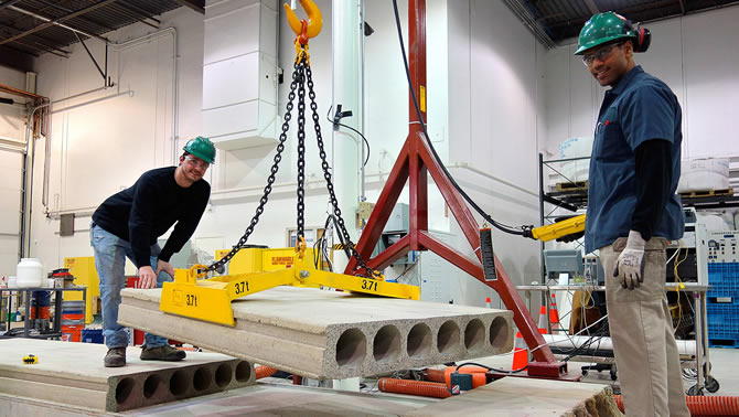 Two men using a crane to hoist a cement block into the air. The cement was hardened using carbon dioxide instead of water.
