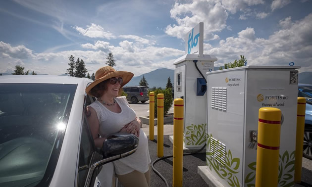 Woman with hat leaning against a charging station. 