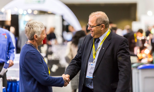 a gentleman at the expo shaking hands with a lady at a booth.