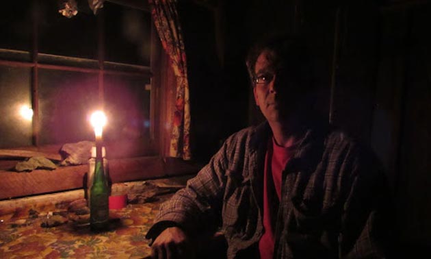 Mortensen sitting beside lit candle in old cabin.