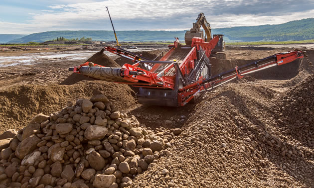 A piece of heavy equipment is moving piles of dirt and rocks.