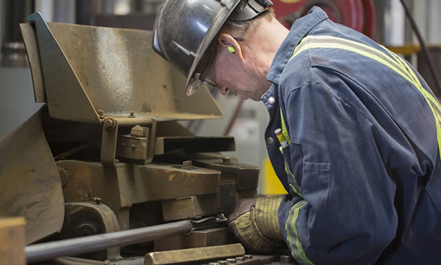 Lifting Services employee grinding a steel rod on a machine. 